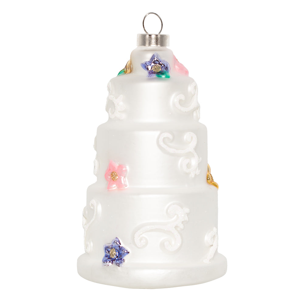 Three-Tiered Wedding Cake ornament. A three-tiered cake with intricate white designs and colorful flowers. View of back.