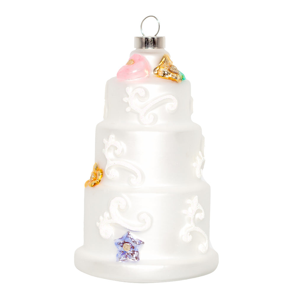 Three-Tiered Wedding Cake ornament. A three-tiered cake with intricate white designs and colorful flowers. View of front.