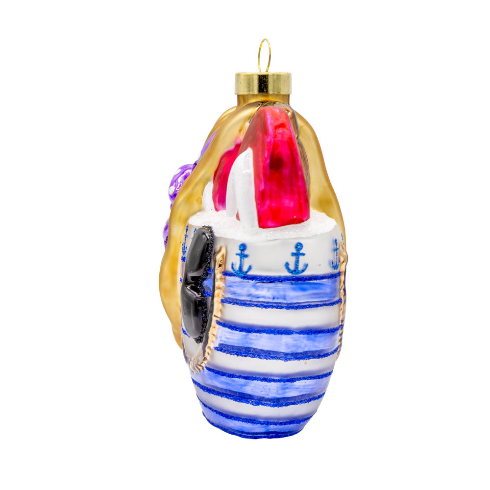 Beach Bag Essentials ornament. A blue striped beach bag holds red flip flops, a pair of shades, and a straw sun hat with a purple bow. View of right side.